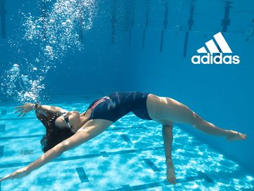 A female swimmer underwater in a pool gracefully leaning back with bubbles rising above her head.