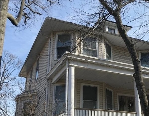 Two-story beige house with white columns and leafless trees.