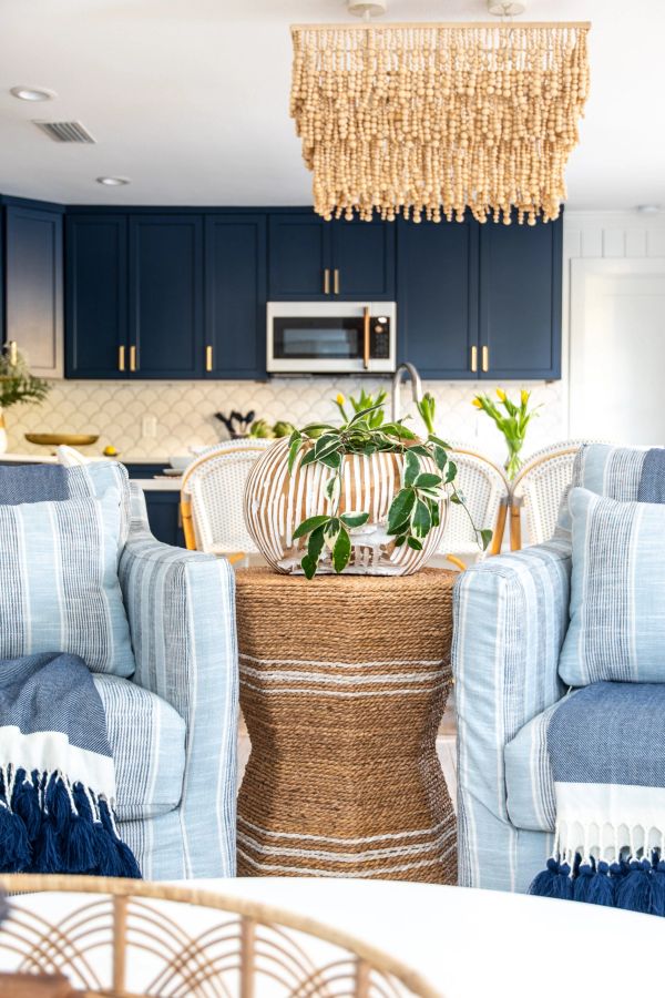 Cozy living space with blue-striped chairs and a woven side table under a beaded chandelier.