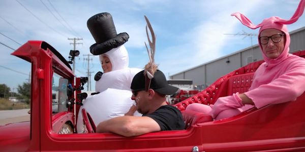 Three people in costumes riding a red car, including a snowman and a pink bunny.