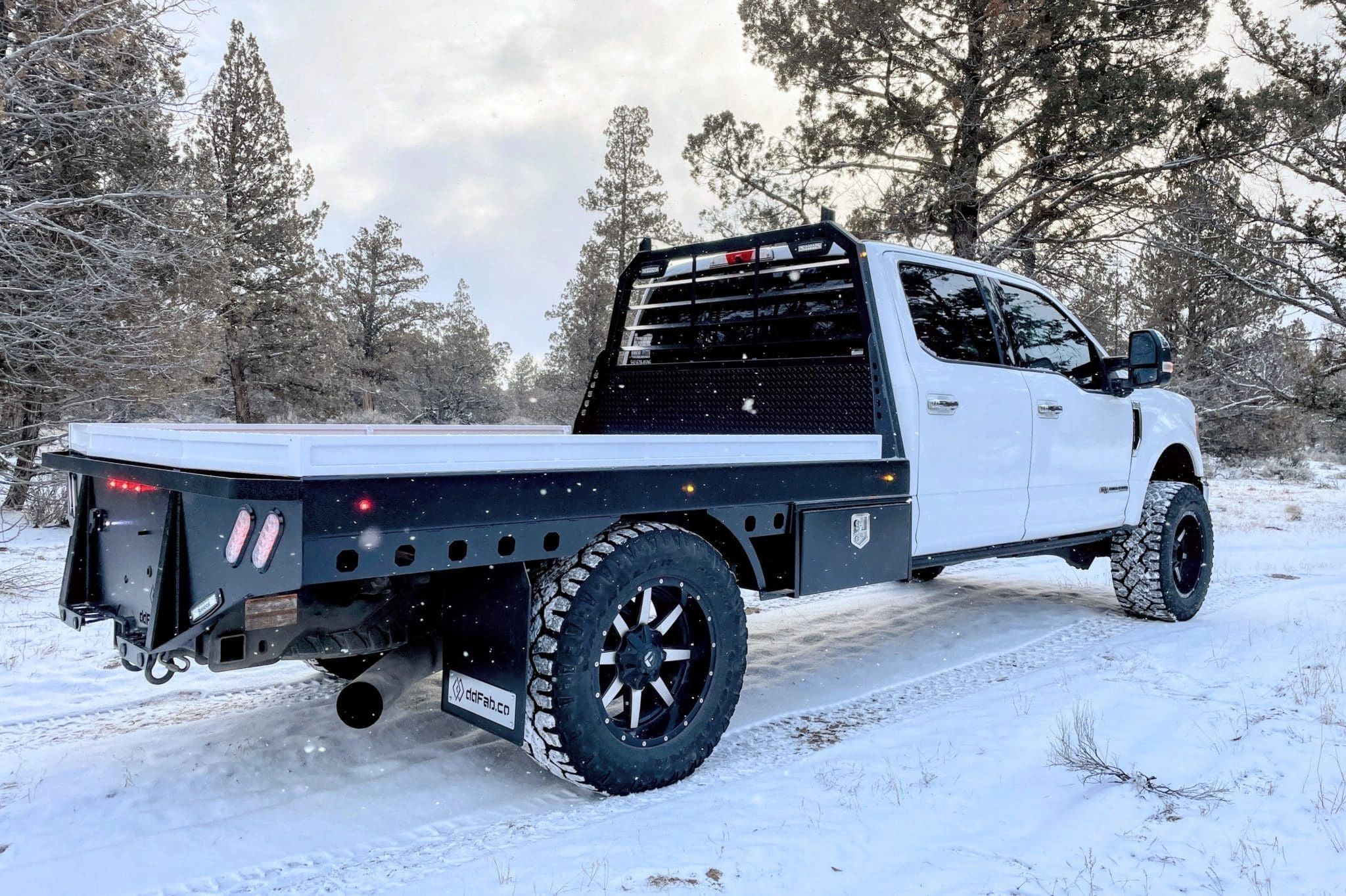 White pickup truck with custom flatbed in snowy forest.