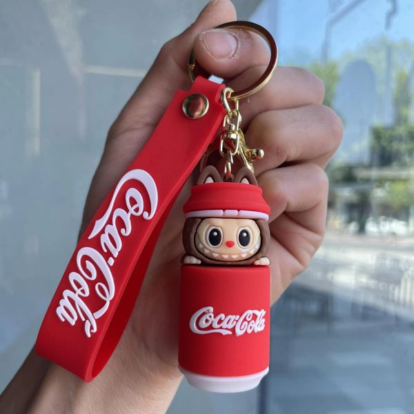 Hand holding a Coca-Cola keychain with a cute character inside a red can.