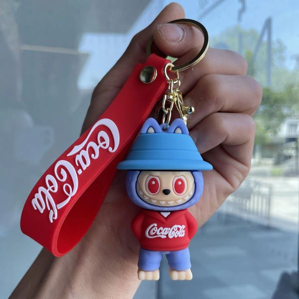 Hand holding a Coca-Cola keychain with a blue-eared character wearing a red hoodie.