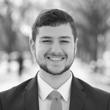 Young man in suit smiling outdoors in black and white.