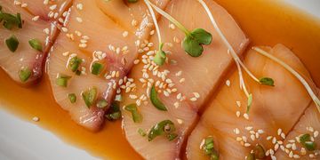 Close-up of sashimi slices garnished with sesame seeds and microgreens in soy sauce.