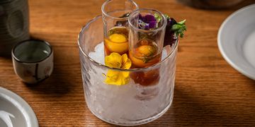 Cocktail glasses with garnishes in an ice bucket on a wooden table.