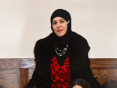 Woman in black hijab and red dress with black fur coat.