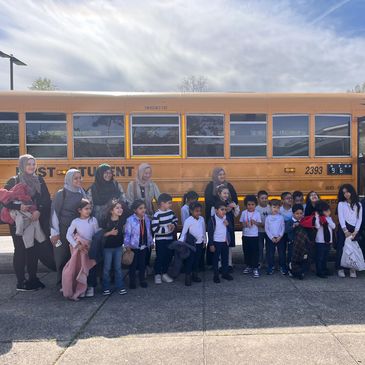 A group of children and adults posing in front of a yellow school bus on a sunny day.