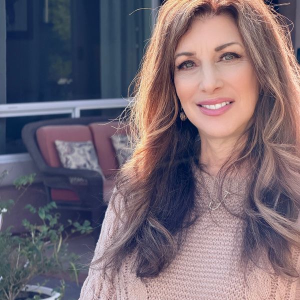A smiling woman with long hair in a cozy sweater outdoors.