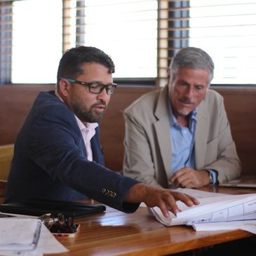 Two men in suits discussing documents at a wooden table.