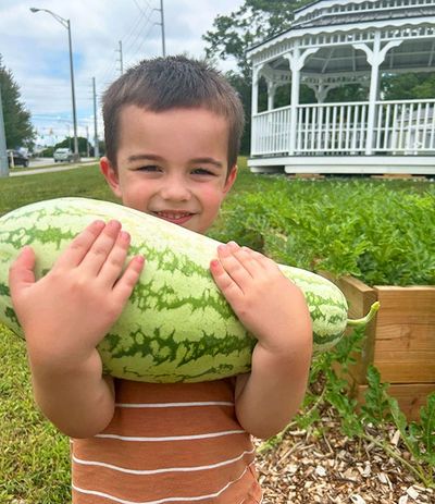 A boy happily holding a large watermelon outdoors.