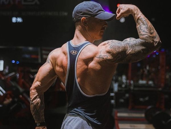 Man flexing his muscular back and arm in gym.