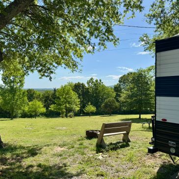 Grassy field with bench and trailer under clear sky.