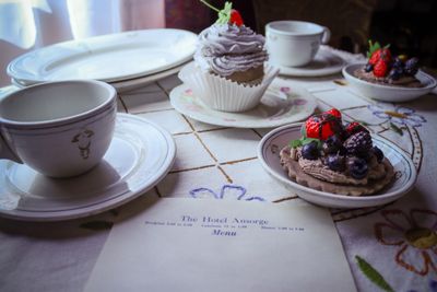 Elegant tea setting with cupcakes and a menu on a floral tablecloth.
