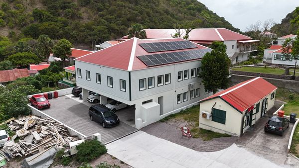 Modern building with solar panels and red roofs in a green hilly area.