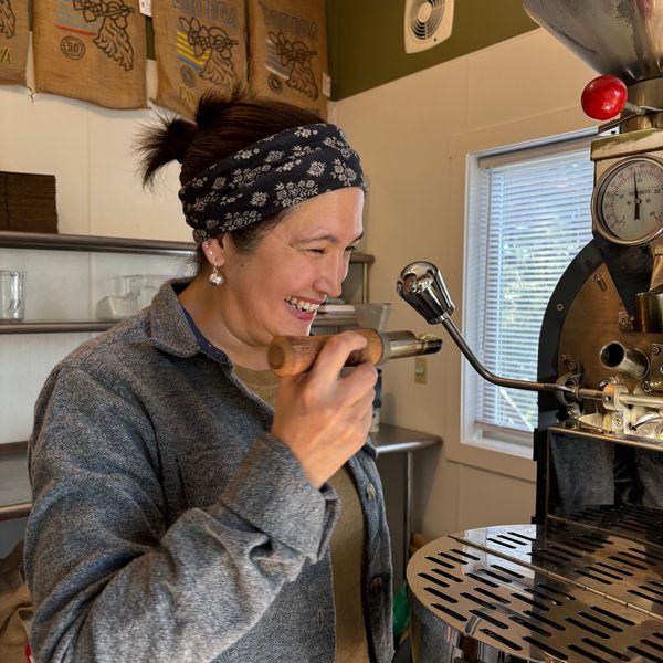 A woman smiling while operating a coffee roasting machine in a cozy room.