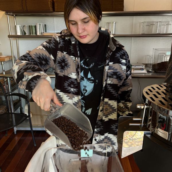 Person pouring coffee beans into a container at a coffee shop.