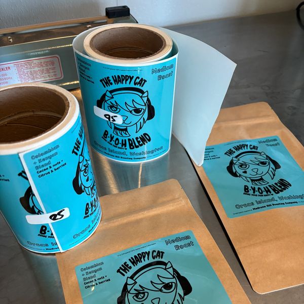 Rolls of blue labels and brown packages for The Happy Cat coffee blend.