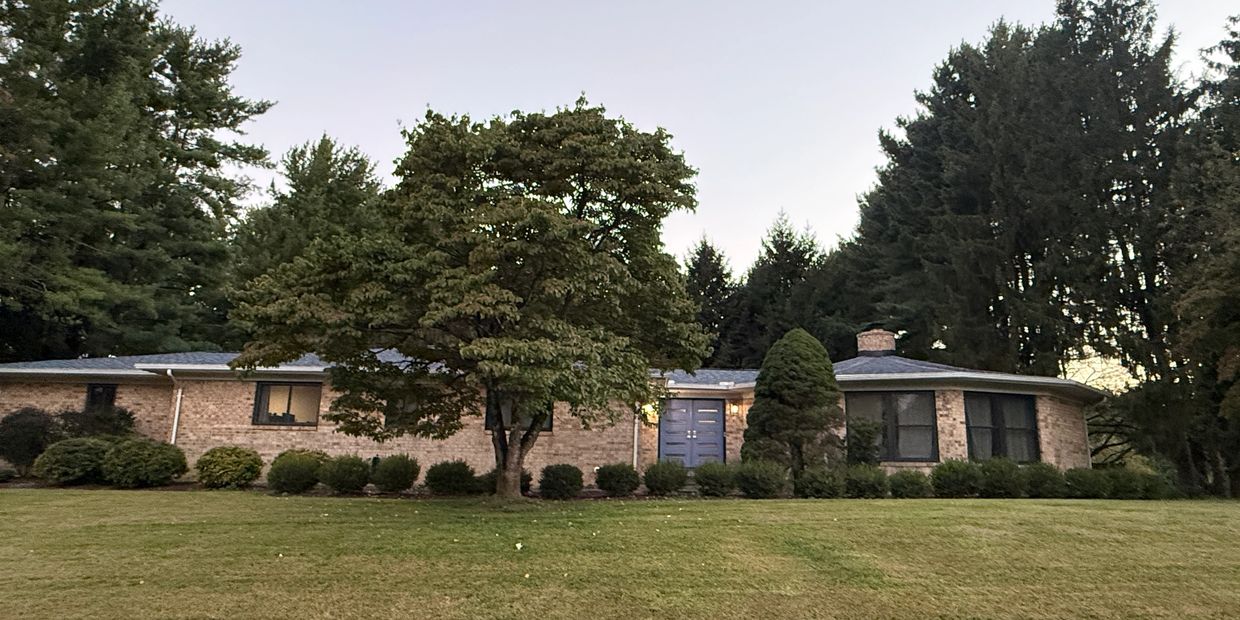 Single-story brick house with trees and lawn.