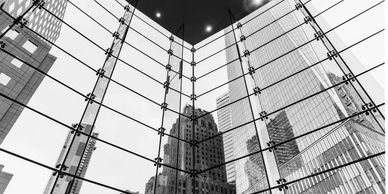 Looking up at skyscrapers through a large glass window in black and white.