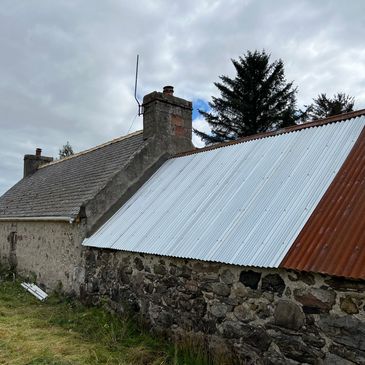 Old stone building with a mixed metal roof under a cloudy sky.