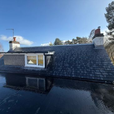 Roof with slate tiles and chimneys under clear sky.