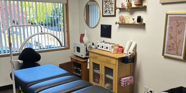A clean, organized medical or therapy treatment room with a black examination table.