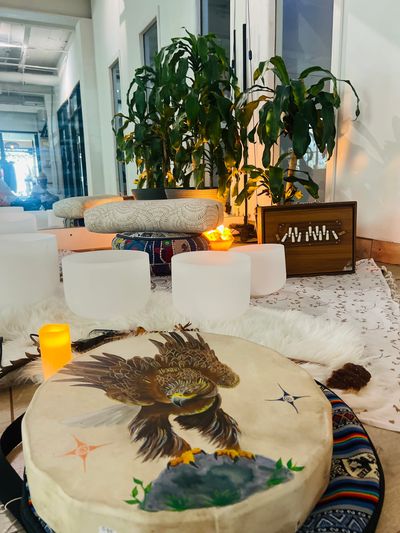 A cozy meditation or relaxation space with plants, cushions, and a drum featuring an eagle design.
