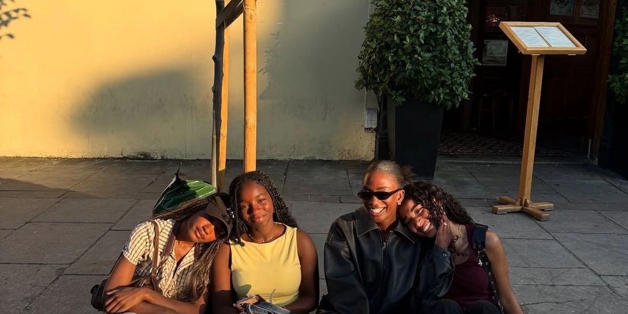 Four friends sitting closely, enjoying a sunny day with warm smiles and relaxed poses.