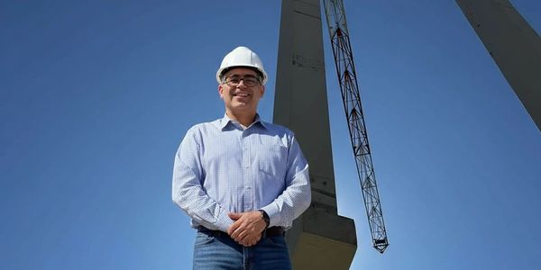 Man in a hard hat standing at a construction site under a clear blue sky.