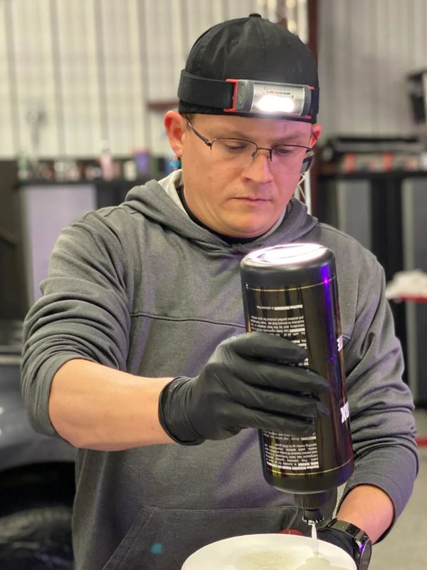 A man inspects and pours liquid from a bottle wearing a headlamp and gloves.
