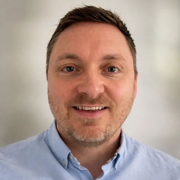 Smiling man with short brown hair and a light blue shirt.
