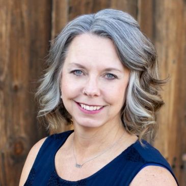 Smiling woman with gray hair and blue eyes.