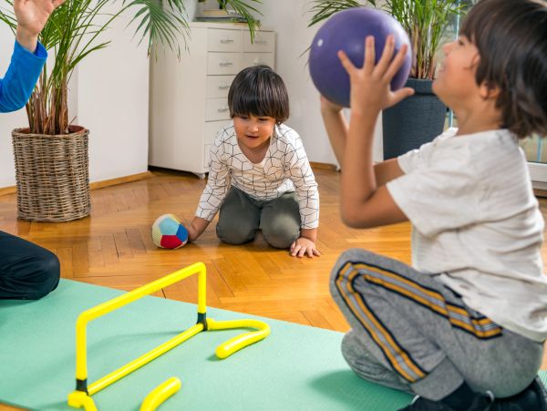 Two boys playing ball indoors near a yellow hurdle.