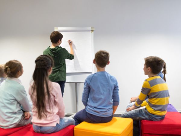 Children in a classroom, one writing on a flip chart.