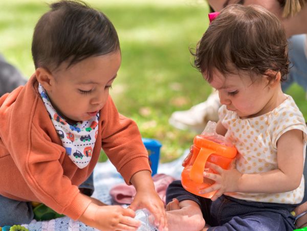Two toddlers playing with cups outside.