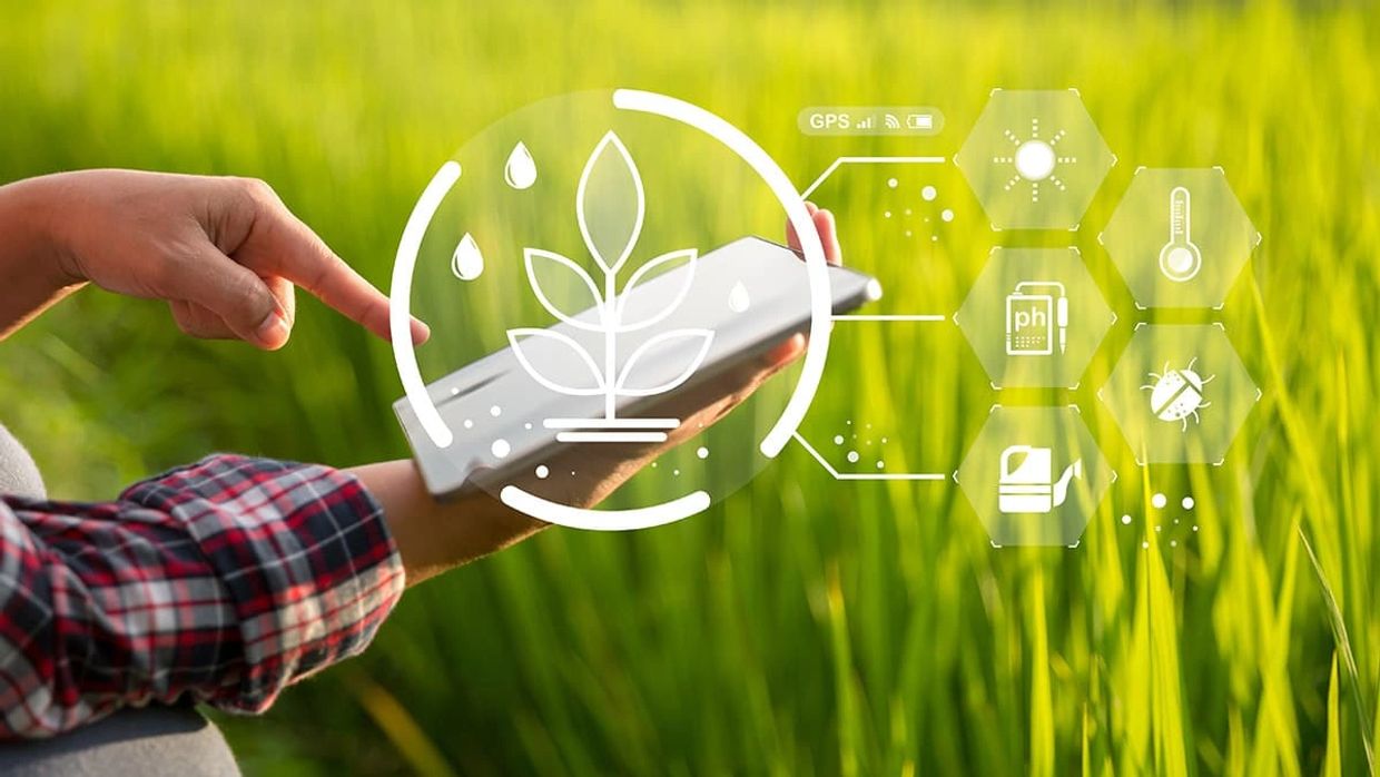 Person using tablet in field with agriculture data overlay icons.