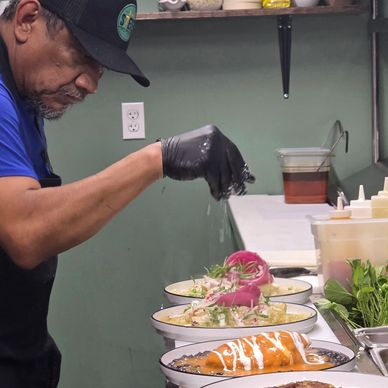 Chef sprinkles seasoning on dishes in a kitchen.