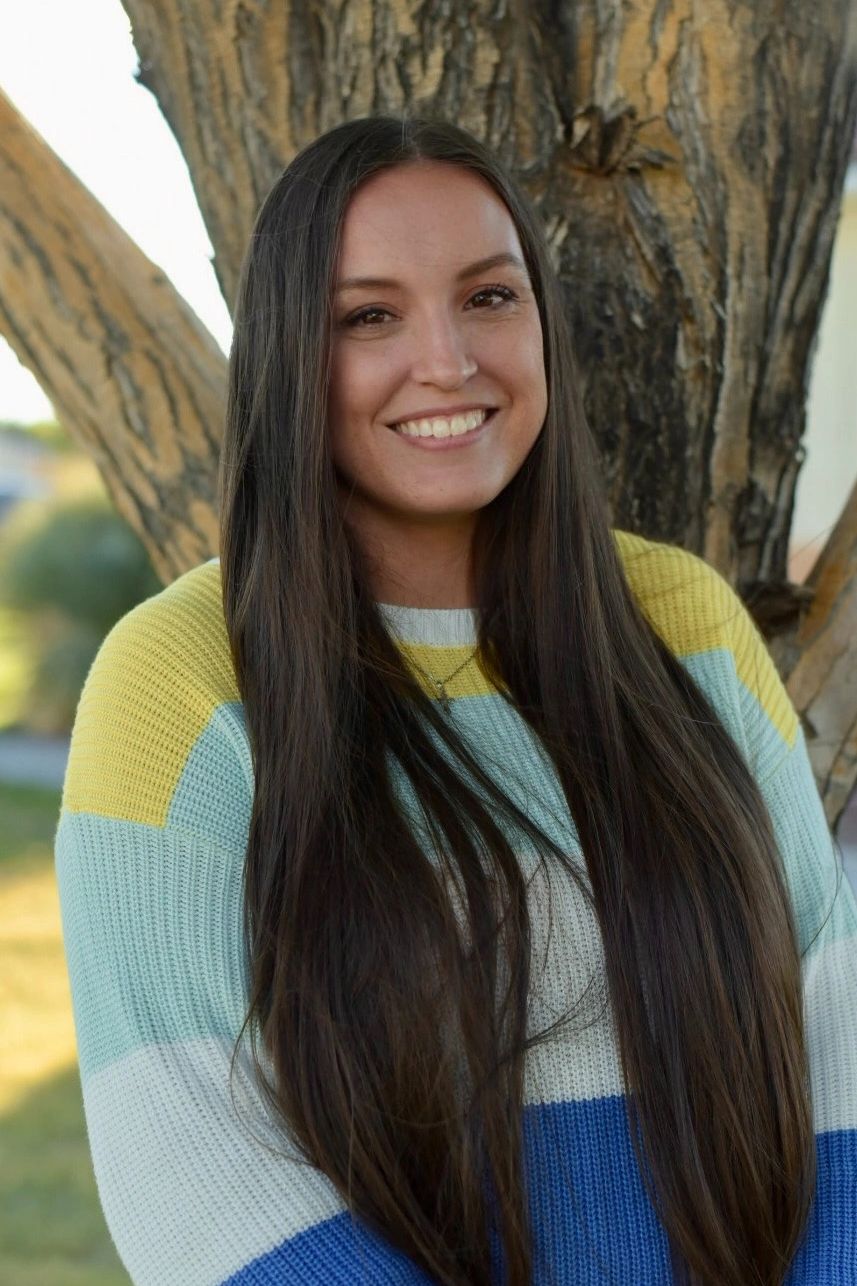 Young woman smiling in a colorful sweater outdoors.