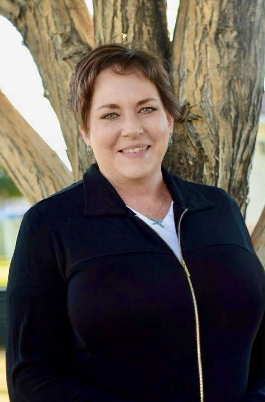 Smiling woman in a black jacket standing by a tree.