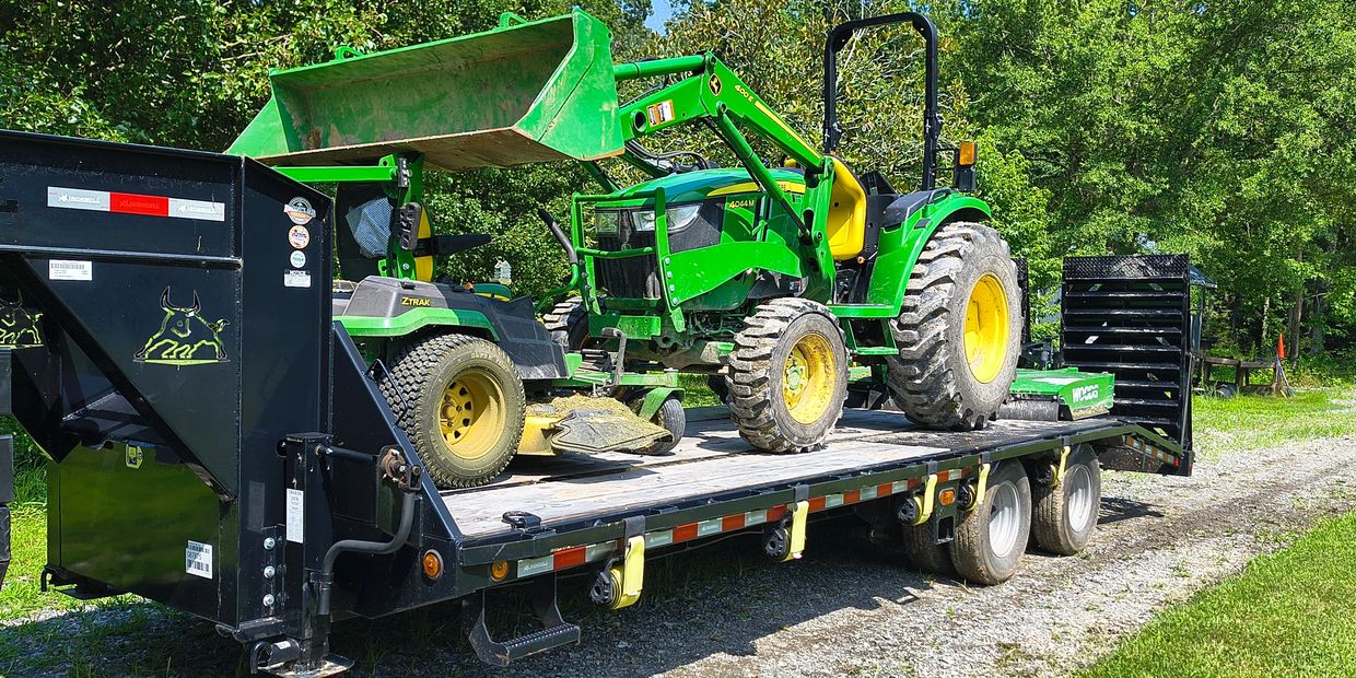 Green tractor and mower loaded on a black flatbed trailer outdoors.