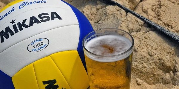 A Mikasa volleyball and a glass of beer on sandy beach.