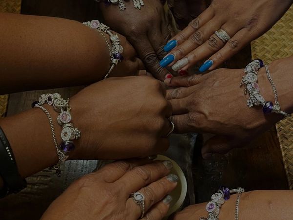 Five hands with matching bracelets and rings joined together in unity.