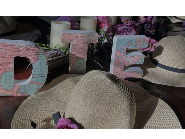 Decorative letters spelling 'DTE' with a map design, surrounded by straw hats and flowers.