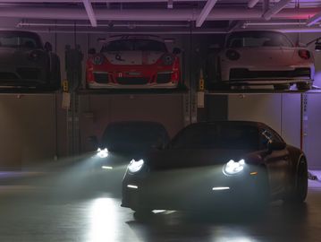 Sports cars with headlights on in a dimly lit garage with elevated platforms.