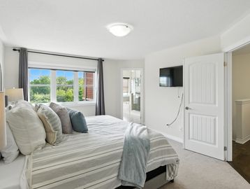Bright bedroom with a large bed, window view, and TV on the wall.