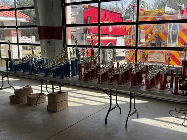 Rows of blue and red trophies displayed on tables inside a fire station.