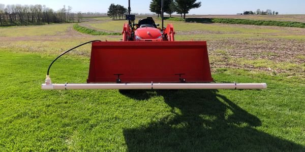 Front view of a red tractor with a mounted PVC pipe sprayer attachment.