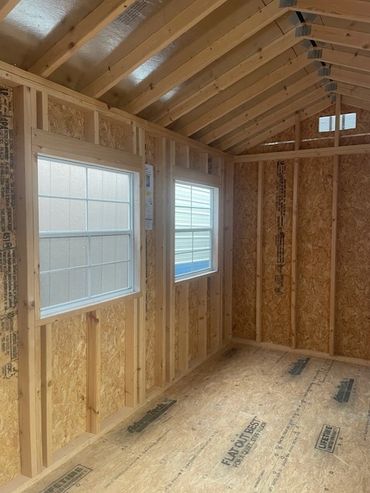 Interior of an unfinished wooden shed with two windows and exposed framing.