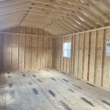 Empty wooden shed interior with sloped roof and window.